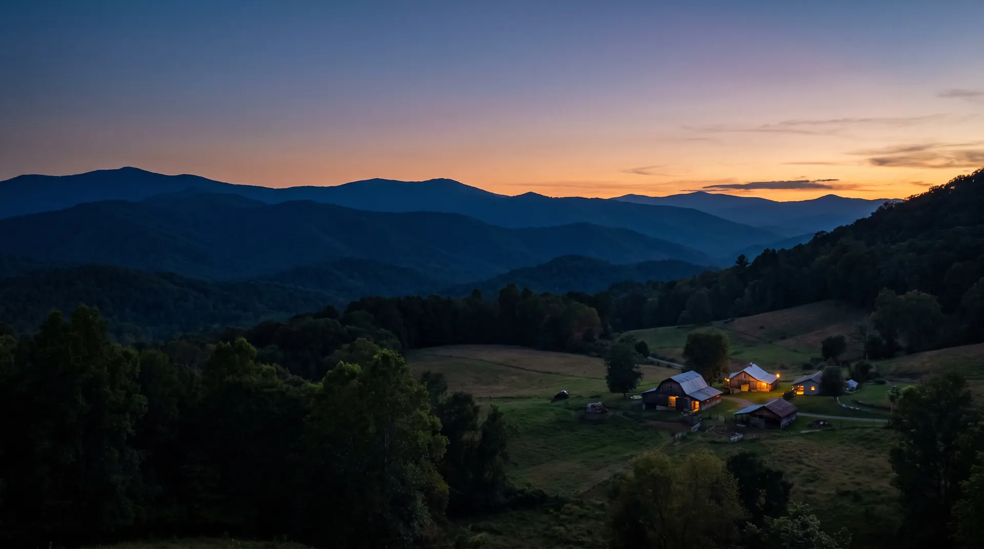 Layered Blue Ridge mountains at dusk above a valley farm with lit windows